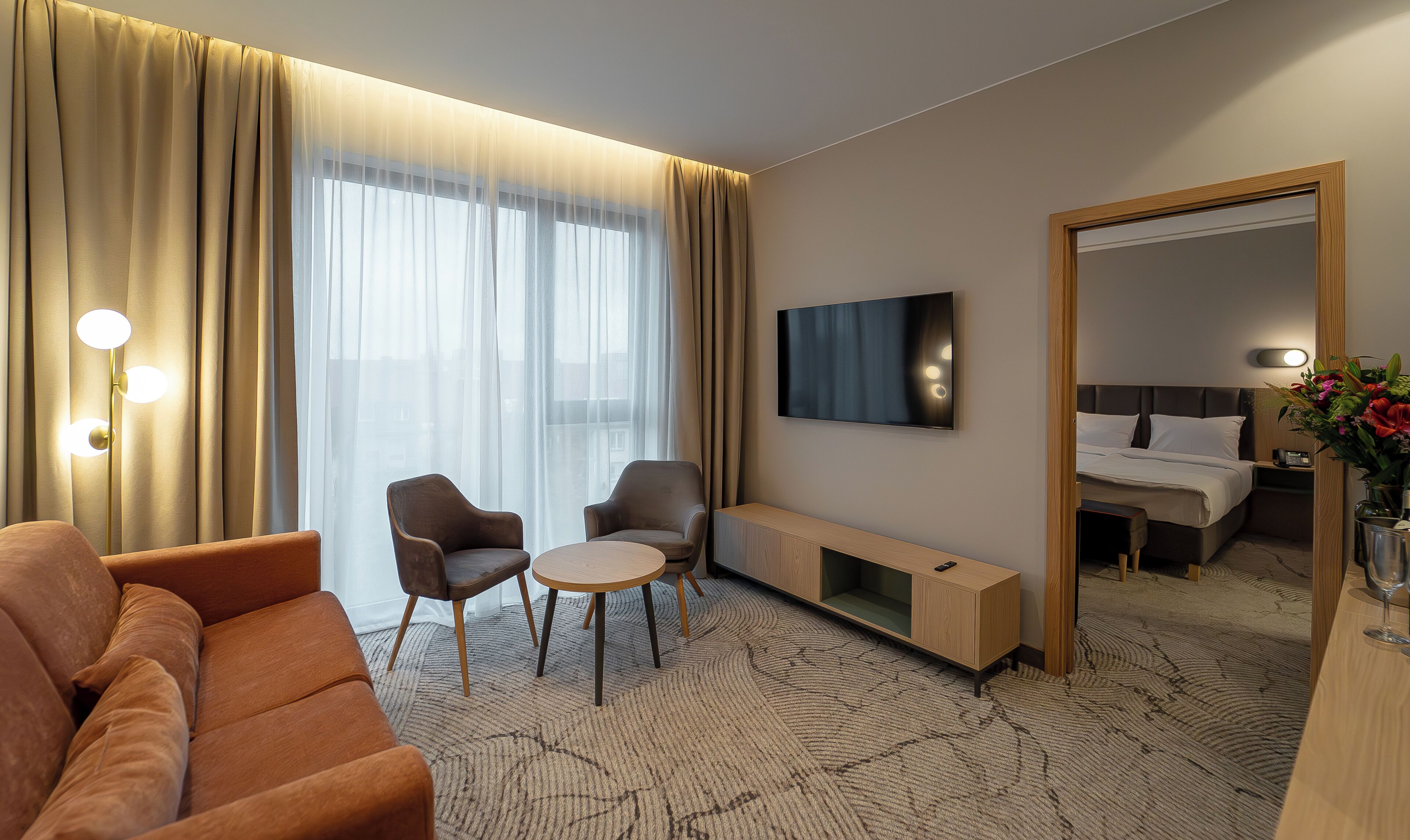 Habitación de hotel con sofá, dos sillones, una mesita, televisor, mesita de noche con lámpara y espejo.