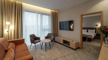Habitación de hotel con sofá, dos sillones, una mesita, televisor, mesita de noche con lámpara y espejo.