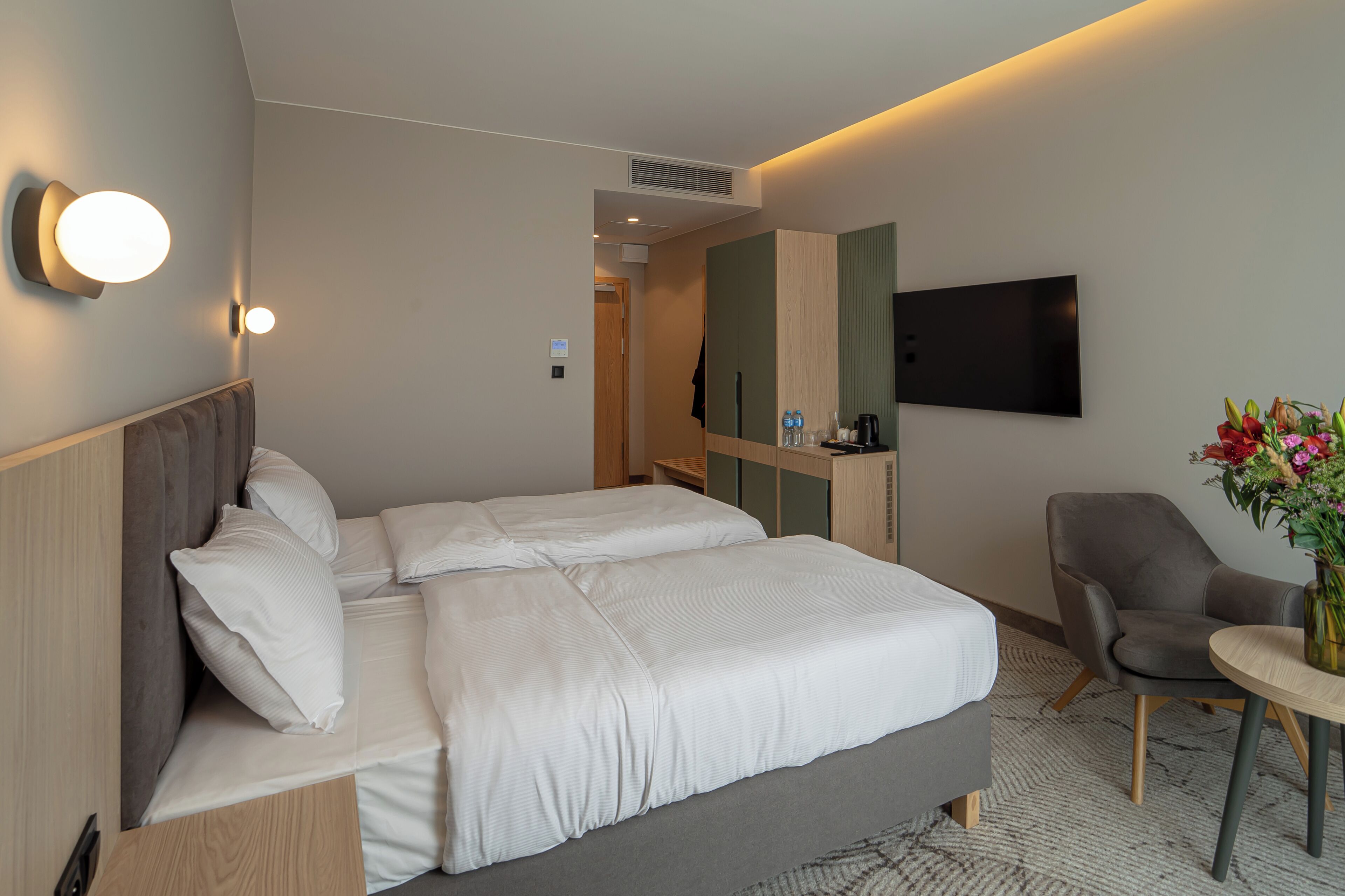 Habitació d'hotel amb llit, una cadira, taula petita, televisió i llum penjada a la paret.