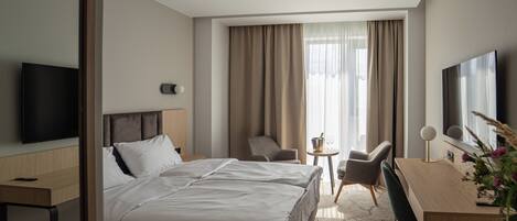 A hotel room with a bed, a desk, a chair, a television, and a window with curtains.