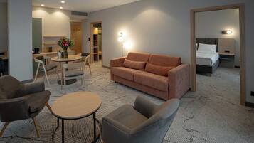 A hotel room with a sofa, armchairs, a small table, a bed, and a bathroom visible through an open door.
