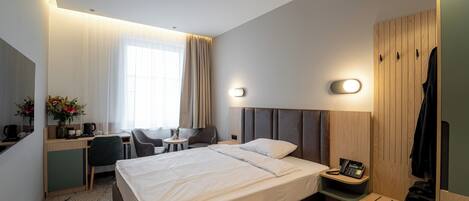 A hotel room with a bed, bedside table, desk, chair, and a wardrobe.