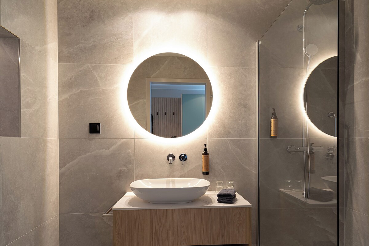 A modern bathroom with a round mirror, a sink, and a glass-enclosed shower.