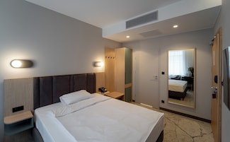 Una habitación de hotel con cama, mesita de noche, lámpara de pared y espejo.