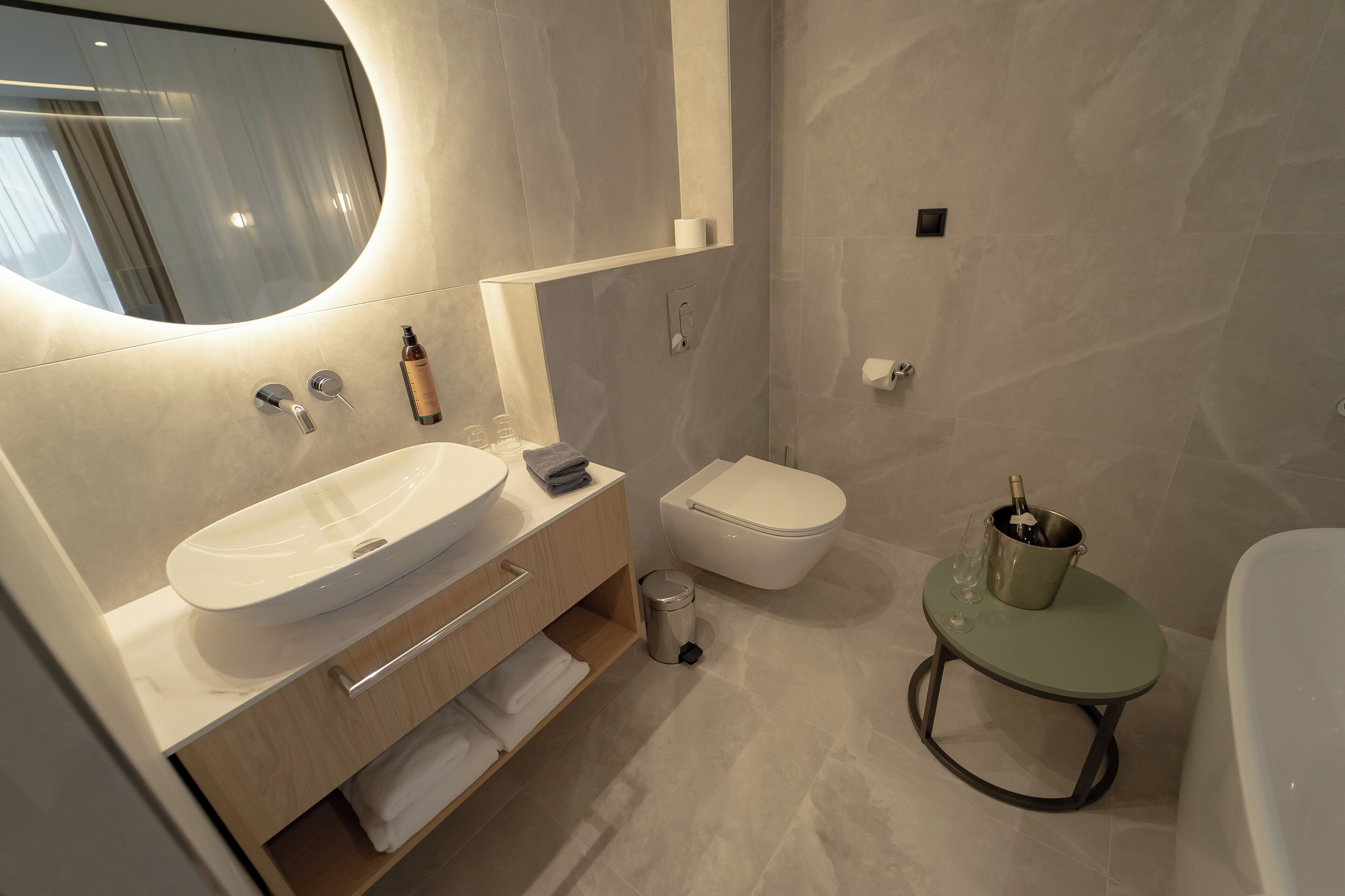 Un baño moderno con un lavamanos grande, inodoro y una pequeña mesa redonda con una botella y vasos.