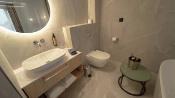 Un baño moderno con un lavamanos grande, inodoro y una pequeña mesa redonda con una botella y vasos.