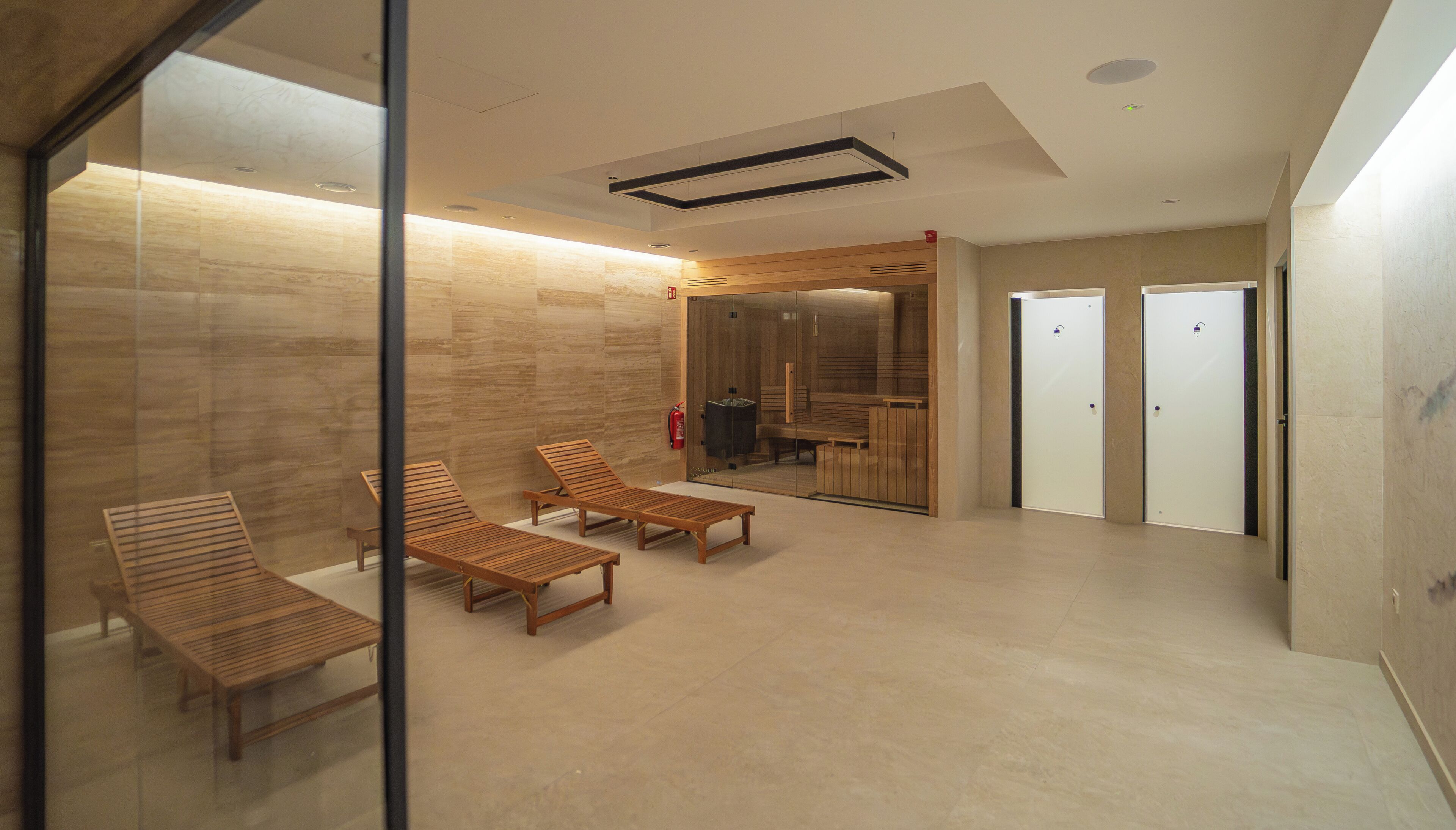 A modern spa area with wooden loungers, a glass partition, and a sauna visible through a glass door.
