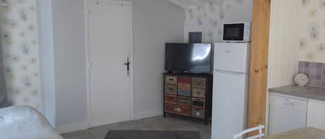 A room with a bed, a table, chairs, a kitchen area with appliances, and a ceiling with exposed beams.
