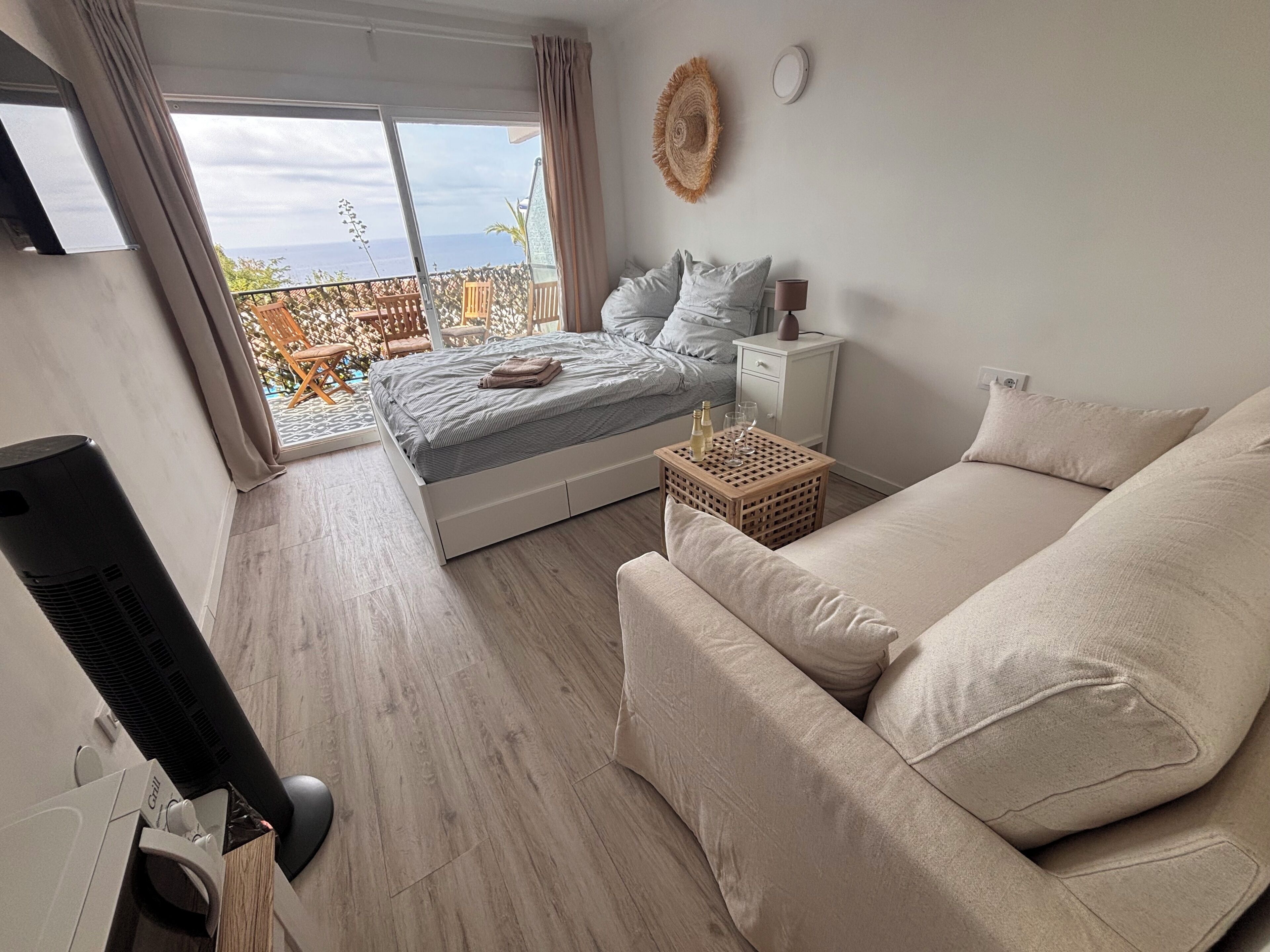 Une chambre avec un lit, une table de chevet avec une lampe, un plancher en bois, un balcon avec vue et un téléviseur.
