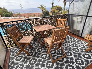 Ein Balkon mit einem gemusterten Boden, Holzstühlen, einem Tisch und Blick aufs Meer.