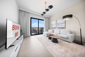 Un soggiorno moderno con una televisione a schermo piatto, un divano, un tavolino, una lampada da terra e un balcone con vista sulla città.