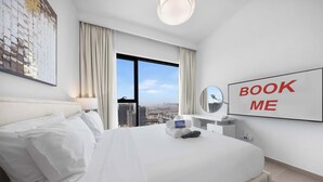 Une chambre d’hôtel avec un grand lit, un bureau avec un miroir, une pancarte indiquant « RÉSERVEZ-MOI » et une vue sur la ville.