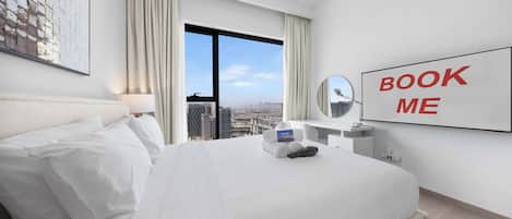 Habitación de hotel con una cama grande, un escritorio con espejo, un cartel que dice 'BOOK ME' y vistas a la ciudad.
