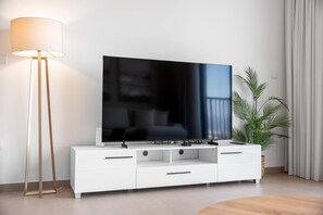A modern living room with a flat-screen TV on a white entertainment unit, a floor lamp, and a potted plant. - StayShort - Chic 1-Bedroom for 4 in Prime Dubai Hills Location! (Dubai Hills)
