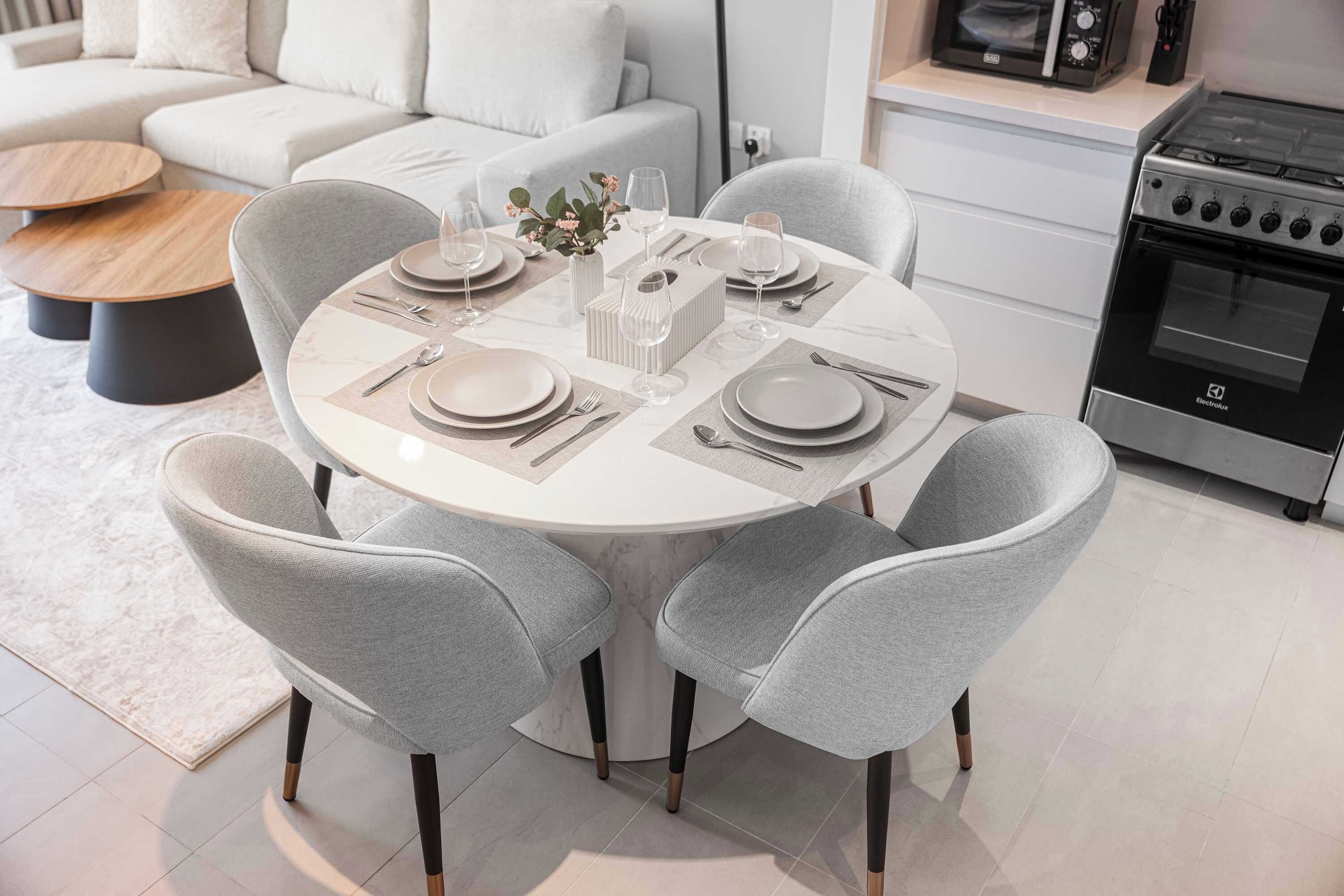 Une cuisine moderne avec une table de salle à manger ronde pour quatre personnes, des chaises à revêtement gris, un four encastré et un micro-ondes posé sur le plan de travail.