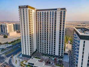Un edificio a grattacielo con un cartello ben visibile 'EMAAR', numerosi balconi e un'area di parcheggio con diverse auto.