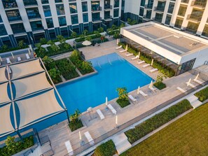 A modern building with a rooftop pool, lounge chairs, and a landscaped garden area. - StayShort - Chic 1-Bedroom for 4 in Prime Dubai Hills Location! (Dubai Hills)