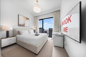 Ein modernes Hotelzimmer mit einem großen Bett, einem Schreibtisch, einem Fernseher und Blick auf die Stadt.