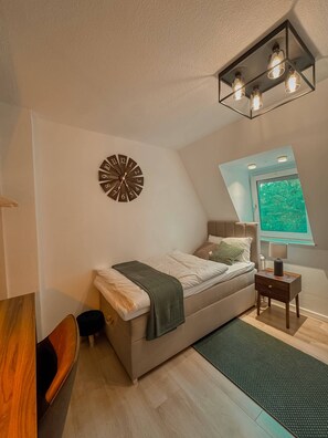 Ein Schlafzimmer mit Bett, Nachttisch, Wanduhr und Fenster mit Blick.