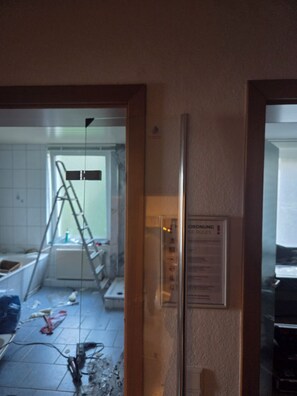 Ein Zimmer mit einer an der Wand angelehnten Leiter, einer Tür mit einem Schild und einem Fenster mit Blick auf ein weiteres Zimmer.