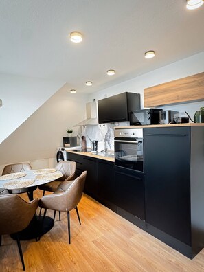 A modern kitchen with a dining area, featuring a built-in oven, microwave, and coffee maker. - Bibo City Suite Apartment (Bielefeld)