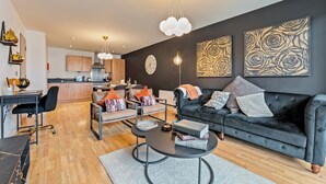 Ein modernes Wohnzimmer mit einem dunklen Sofa, einem Couchtisch und einem Essbereich im Hintergrund.