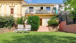 Un edificio residenziale con un balcone, un muro in pietra e un prato con due poltrone da relax.