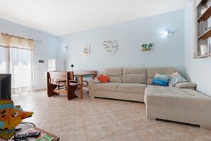 A living room with a sofa, a dining table with chairs, a television, and a window with curtains.