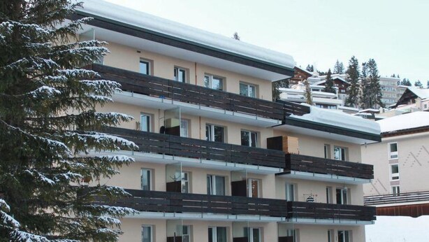 Un hotel de varios pisos con balcones, un techo cubierto de nieve y un pino al frente.