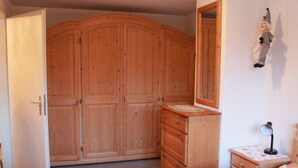 Un dormitorio con un armario de madera, un tocador, una cama con colcha estampada y una mesita de noche con lámpara.