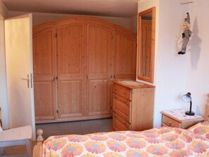 A bedroom with a wooden wardrobe, a dresser, a bed with a floral bedspread, and a bedside table with a lamp. - Haus Seewaldweg 309 Appartement/Fewo,  , 3-Bettwohnung 3-Bettwohnung by Interhome (Arosa)