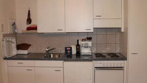 Una cocina compacta con armarios blancos, un lavamanos, una estufa y un microondas.