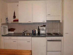 A compact kitchen with white cabinets, a sink, a stove, and a microwave. - Haus Seewaldweg 309 Appartement/Fewo,  , 3-Bettwohnung 3-Bettwohnung by Interhome (Arosa)