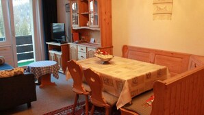 Un comedor acogedor con una mesa, sillas y un banco. Se observa un televisor y un mueble en el fondo.