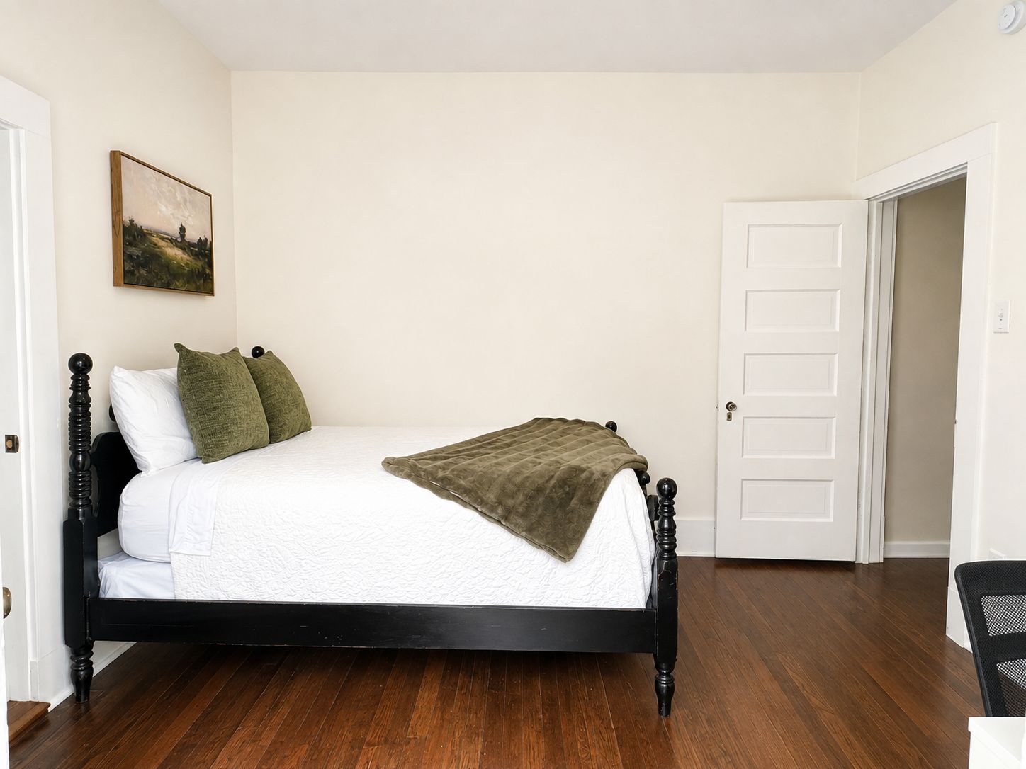 Een slaapkamer met een bed, een deur en een schilderij aan de muur.