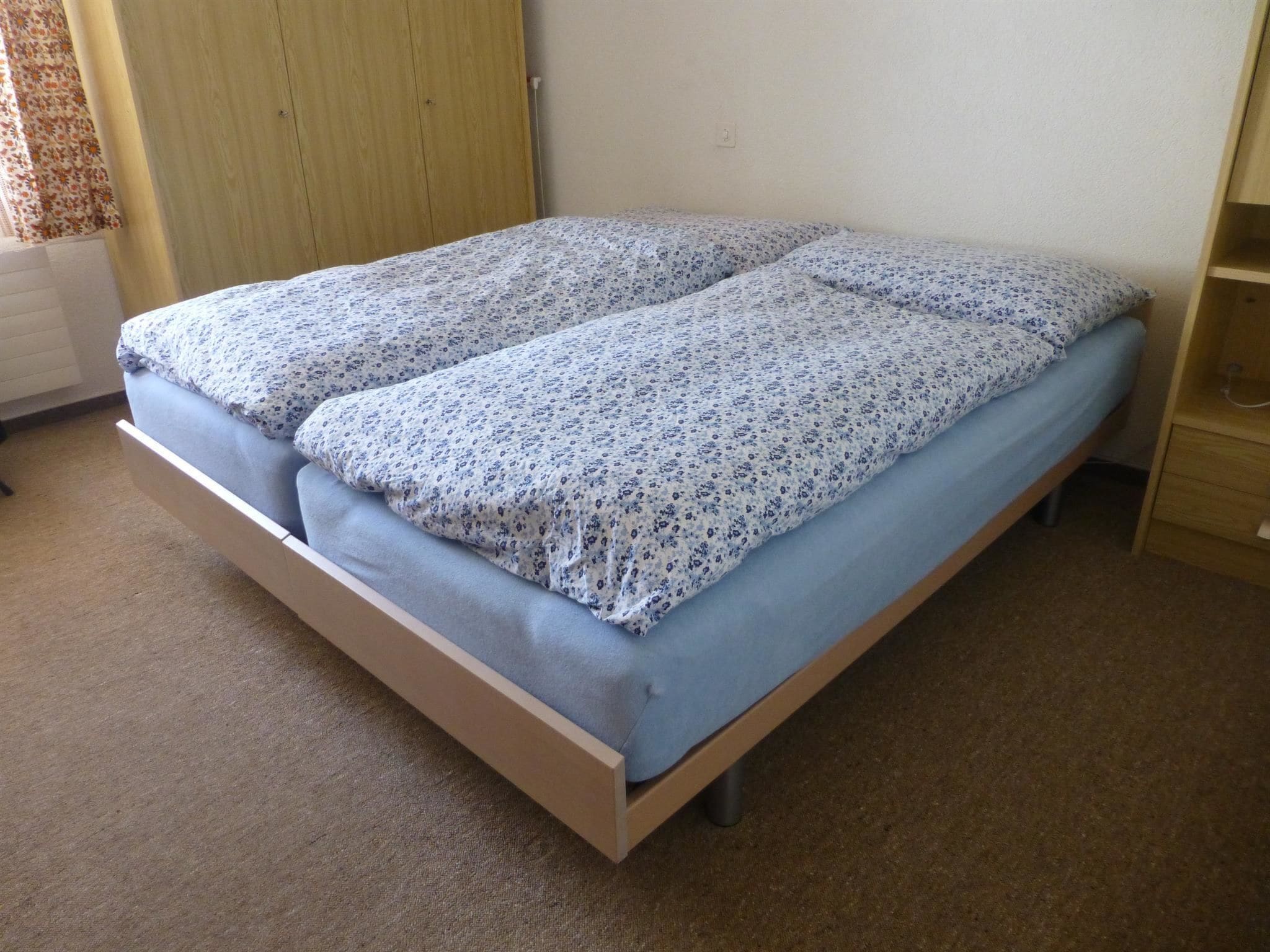 Een eenpersoonsbed met een bloemenbedekker en bijpassend kussen in een kamer met een houten kledingkast en een radiator.