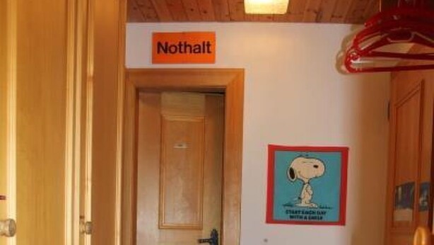 En hall med trädörrar, en skylt med texten ”Nothalt” ovanför en dörr och en Snoopy-affisch på väggen.