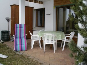 Eine Terrasse mit Tisch, Stühlen und einem gestreiften Kissen, sowie einer Tür.