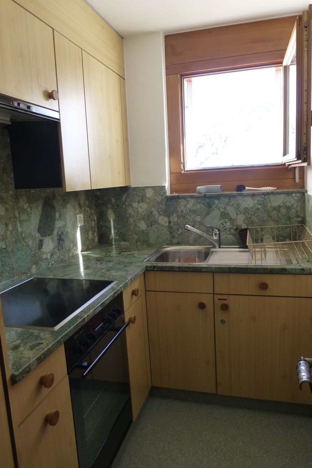 Une cuisine avec des meubles en bois, un plan de travail en granit, une cuisinière encastrée et une fenêtre au-dessus de l’évier.