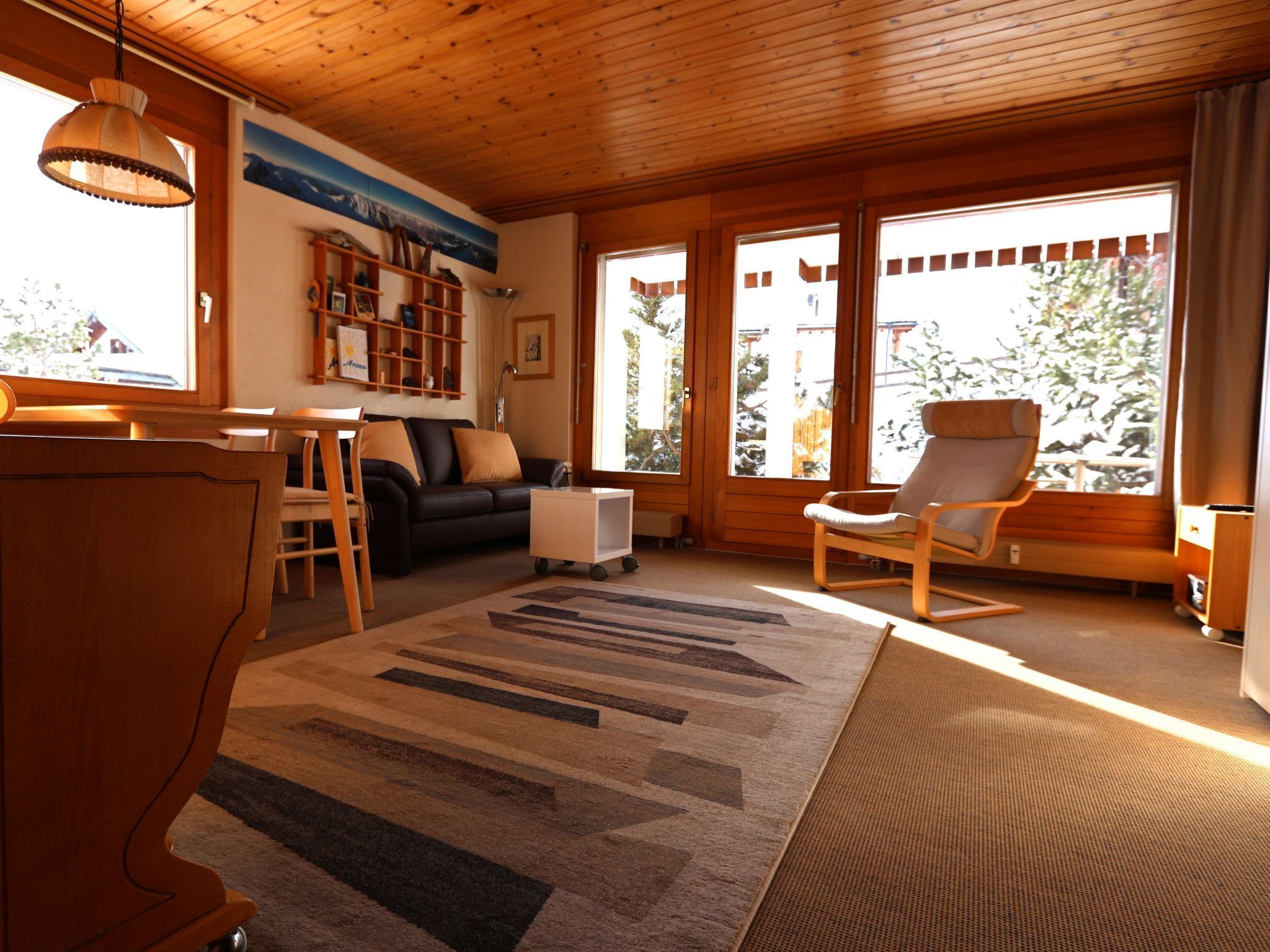 Een gezellige woonkamer met een houten plafond, een bank, een salontafel, een boekenkast en een fauteuil.
