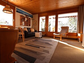 A cozy living room with a wooden ceiling, a sofa, a coffee table, a bookshelf, and a chair.