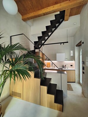 Eine moderne Küche mit einer zentralen Kochinsel, einer Treppe mit schwarzen Geländern und einer Holzbalkendecke.