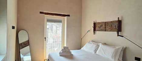 Ein Schlafzimmer mit einem Bett, einem Nachttisch, einem Spiegel und einer Tür zu einem Außenbereich.