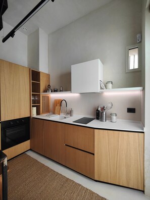 Eine moderne Küche mit Holzschränken, einem schwarzen Ofen, einer weißen Arbeitsplatte und einem integrierten Spülbecken.