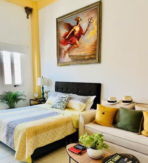 A bedroom with a bed, a nightstand, a lamp, a sofa, a coffee table, a potted plant, and a framed artwork on the wall. - Cozy Studio Apt. in charming Cartagena with AC (Cartagena)