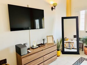 A modern living room with a flat-screen TV mounted on the wall, a wooden cabinet with a mirror, and a potted plant. - Cozy Studio Apt. in charming Cartagena with AC (Cartagena)
