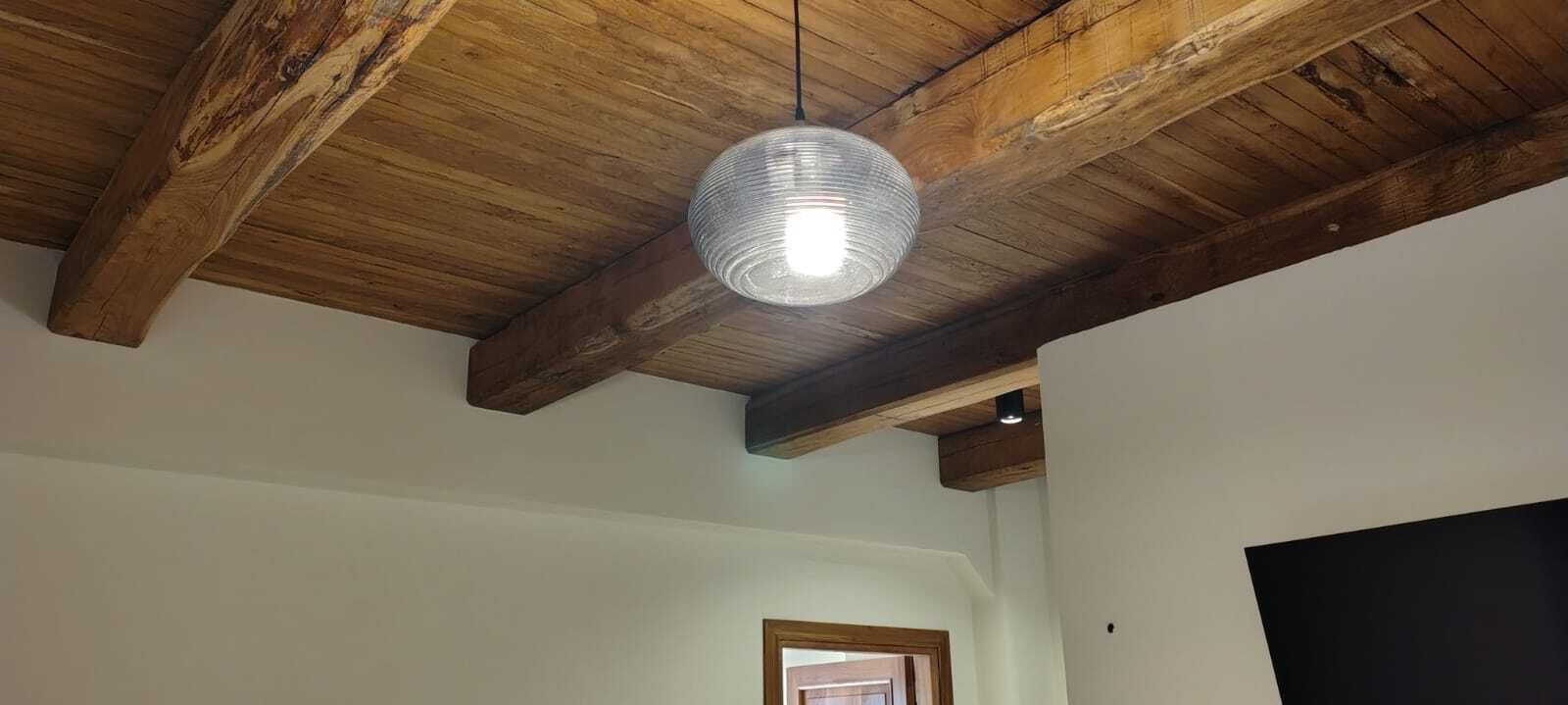 Una habitación con vigas de madera a la vista, una lámpara colgante y una puerta al fondo.