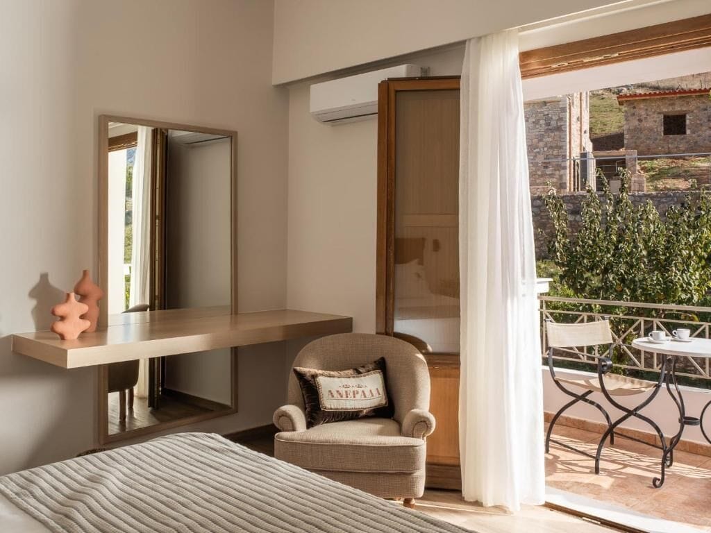 Un dormitorio con cama, una silla, una mesita de noche, un espejo y un balcón con mesa y sillas.