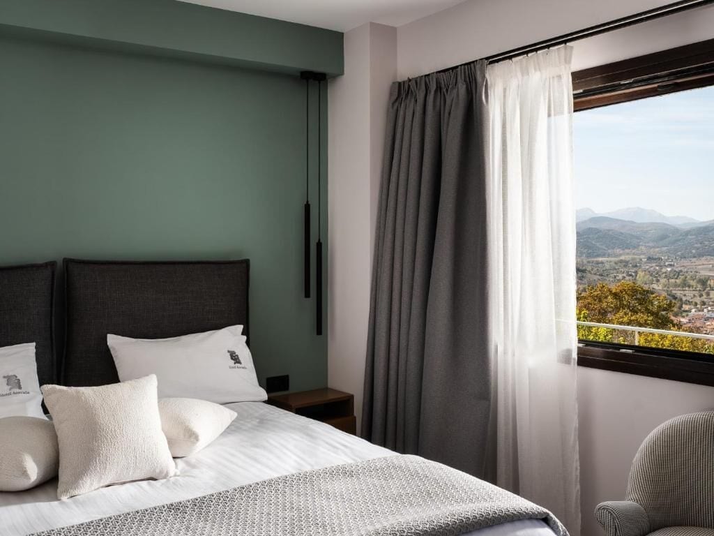 Una camera d'albergo con un letto, un comodino, una sedia e una finestra con tende.