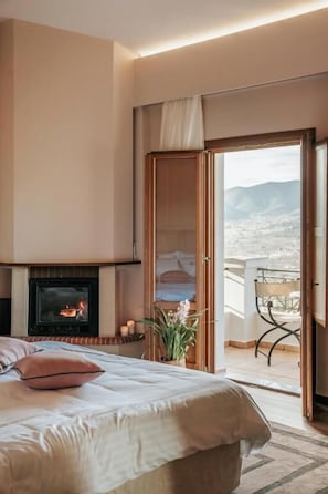 Un dormitorio con cama, chimenea, balcón con una silla y vistas al exterior.